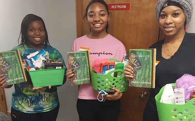 Three young women smiling and holding baskets filled with toiletries